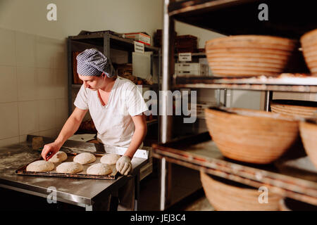 Un Baker fa incisioni manuale sull'impasto per il pane. La produzione di pane.panificio Foto Stock