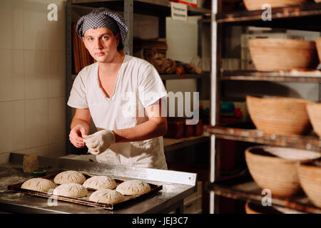 Un Baker fa incisioni manuale sull'impasto per il pane. La produzione di pane.panificio Foto Stock