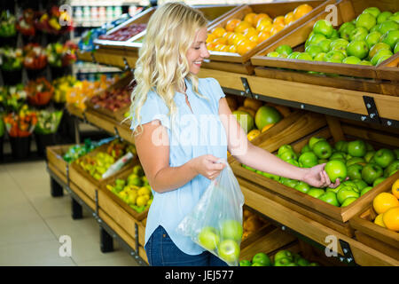 Donna sorridente mettendo le mele in un sacchetto di plastica Foto Stock