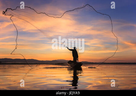 Silhouette pescatore sulla barca da pesca impostazione net con sunrise Foto Stock