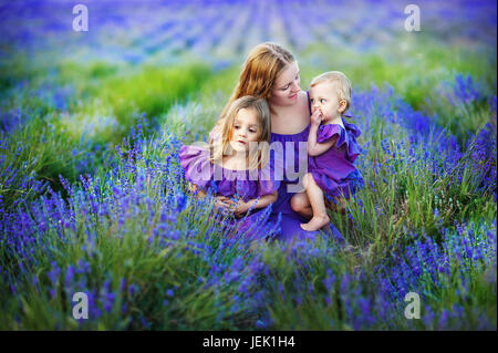 Ritratto di famiglia - la madre e le sue due figlie in un bellissimo pavimento di lavanda. Concetto di una forte bella famiglia, amicizia e fiducia Foto Stock