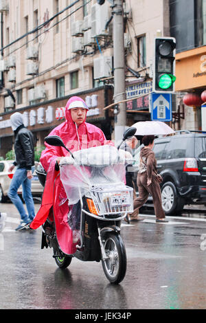 Donna cinese vestito di pioggia-usura su un e-bike. Shanghai è un umido clima subtropicale, con acquazzoni occasionali o temporali. Foto Stock