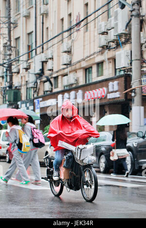 Chinese Boy vestito di antipioggia su un e-bike. Shanghai è un umido clima subtropicale, l'estate è molto caldo e umido. Foto Stock