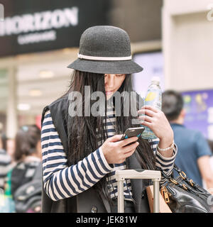 PECHINO-21 MAGGIO 2016. Giovane ragazza cinese alla moda occupata con smartphone all'interno di un centro commerciale occupato. Foto Stock