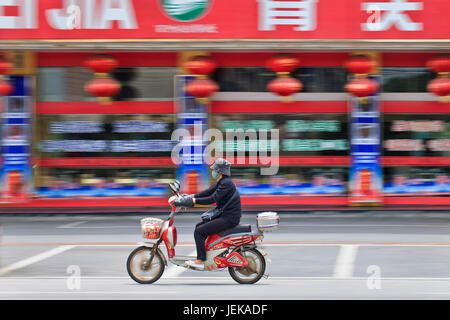 SHANGHAI – 28 MAGGIO. Donna mascherata su una bicicletta elettrica. Almeno 120 milioni di e-bike sono già su strade cinesi, e le vendite sono solo in crescita. Foto Stock