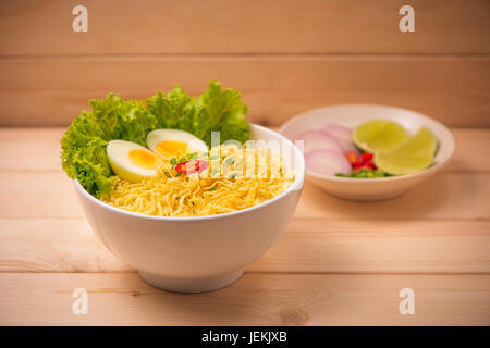 Tagliatelle istante nella ciotola con le verdure e uova sode o su uno sfondo di legno Foto Stock