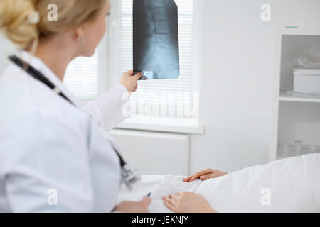 Medico donna esamina un X-ray immagine della colonna vertebrale accanto al paziente sdraiato sul letto in ospedale. Foto Stock