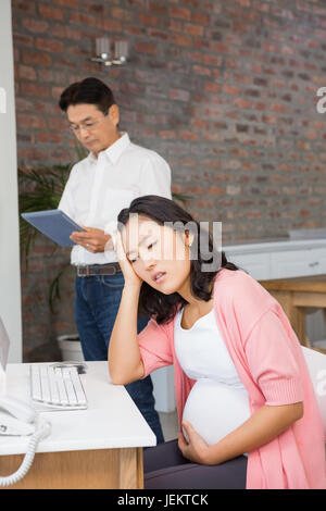La sofferenza donna incinta seduto alla scrivania Foto Stock