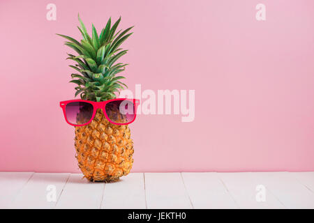 Funny ananas in un paio di occhiali da sole sul tavolo su sfondo rosa Foto Stock