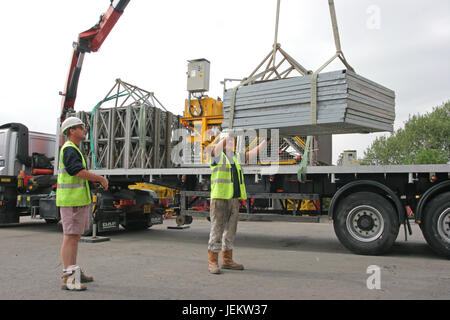Due operai scaricare attrezzature da costruzione da un camion che mostra prassi sicura, lavorando dal livello del suolo. Foto Stock