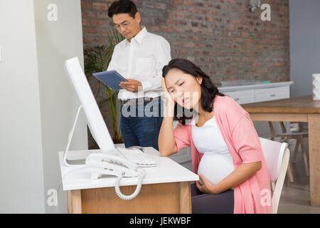 La sofferenza donna incinta seduto alla scrivania Foto Stock