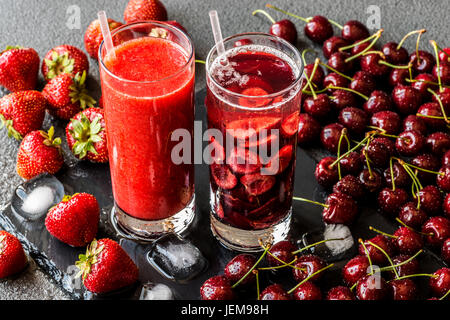 Fragole fresche e smoothie Detox acqua con ciliegie in due bicchieri su sfondo grigio. Una sana detox bevande. Foto Stock