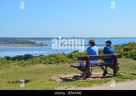 Giovane seduto su un banco di lavoro godendo la vista sul porto di Christchurch da Hengistbury Head, DORSET REGNO UNITO Inghilterra Foto Stock