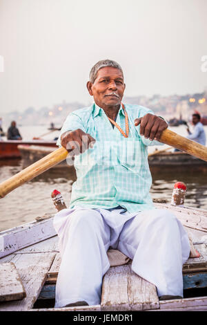 Un uomo indiano remare una barca per escursioni sul fiume Gange, Varanasi (India). Foto Stock