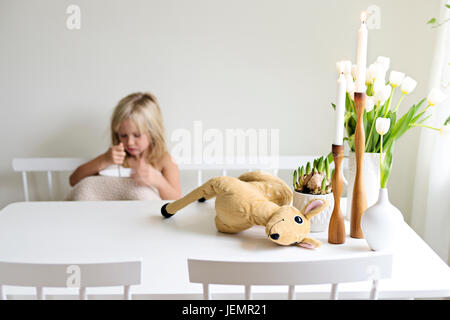 Il giocattolo di peluche, candele e fiori su tavola, ragazza sullo sfondo Foto Stock