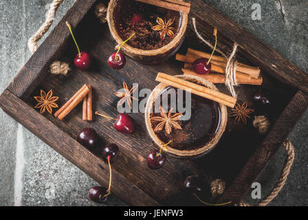 Autunno e Inverno bevande. Hot cherry sangria con cannella, anice, vino e spezie. Su di una pietra scura e lo sfondo di legno con ingredienti, copia spac Foto Stock