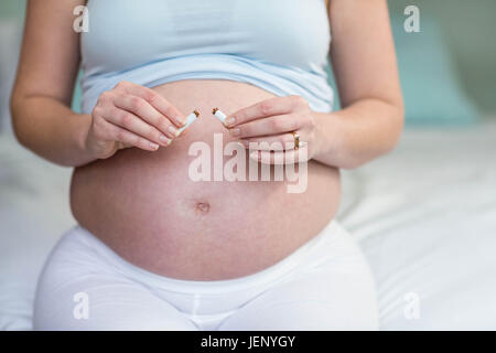 Donna incinta il taglio di una sigaretta in due Foto Stock