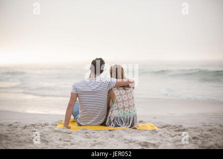 Vista posteriore del giovane seduto sulla spiaggia Foto Stock