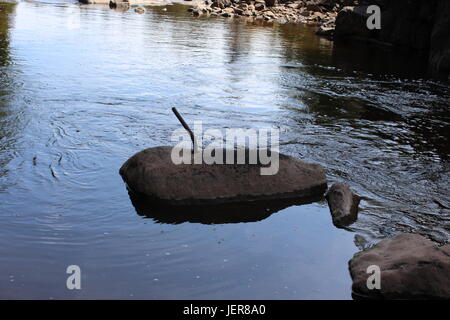 La cattura di immagini di una pietra in un fiume con un tubo di metallo fuori di esso. Effetti di esseri umani sulla natura. Foto Stock