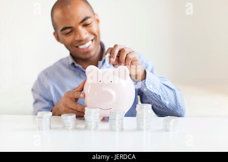 Giovane uomo mettendo in moneta piggybank Foto Stock