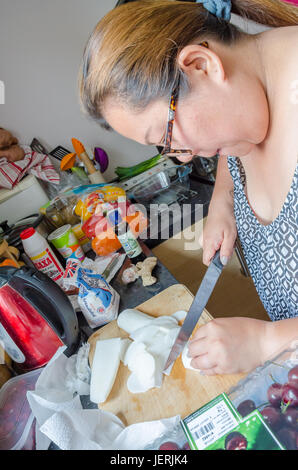 Una donna trita il radicchio bianco in una cucina con un coltello affilato su un tagliere di legno. Foto Stock