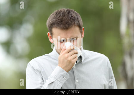 Vista frontale di un uomo che soffia in un panno all aperto con uno sfondo verde Foto Stock