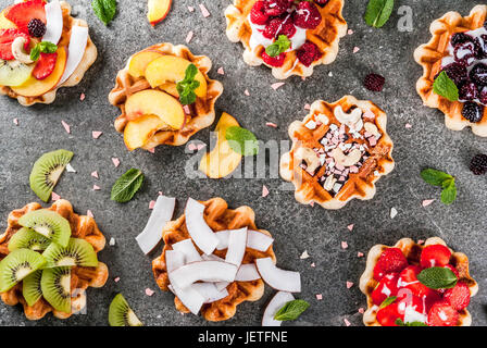 Set di fresco morbido belga di wafer con diversi condimenti - peach, more, lamponi e fragole, noce di cocco, anacardi, fragole e menta. Nero Foto Stock