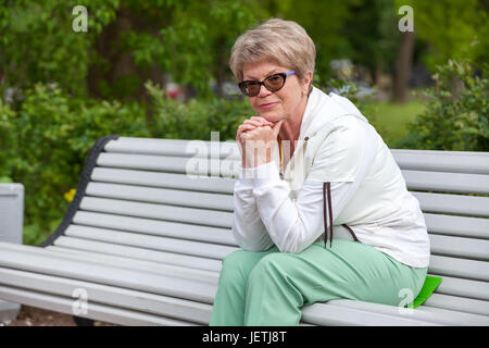Sorridente donna europea in una tuta sportiva è in appoggio su una panchina nel parco Foto Stock