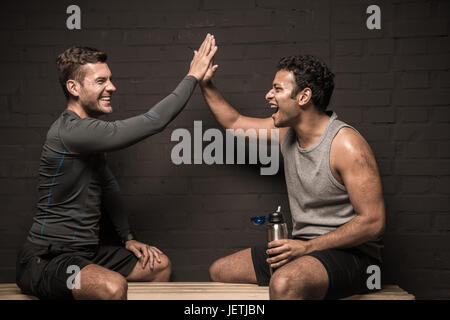 Belli gli atleti maschili in appoggio e conversare in palestra spogliatoi Foto Stock