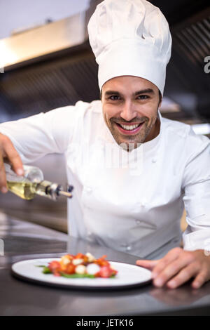 Bello chef versando olio d'oliva sul pasto Foto Stock