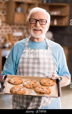 Senior uomo grembiule nella vaschetta di contenimento di deliziosi biscotti, cottura in concetto di cucina Foto Stock