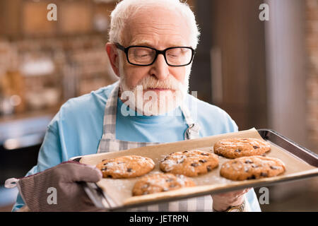 Senior uomo grembiule nella vaschetta di contenimento di deliziosi biscotti, cottura in concetto di cucina Foto Stock