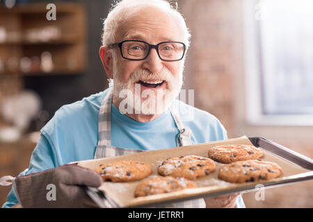 Senior uomo grembiule nella vaschetta di contenimento di deliziosi biscotti, cottura in concetto di cucina Foto Stock