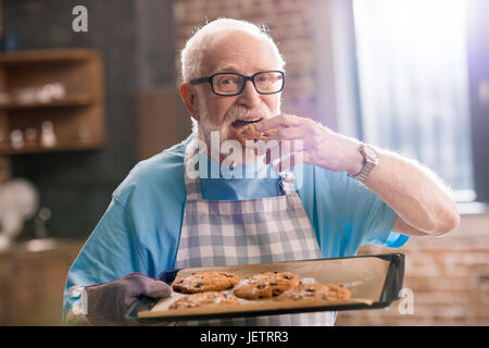 Senior uomo grembiule nella vaschetta di contenimento di deliziosi biscotti, cottura in concetto di cucina Foto Stock