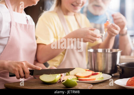 Ritagliato shot della famiglia mele di taglio e preparazione impasto per la torta di mele sul tavolo da cucina Foto Stock