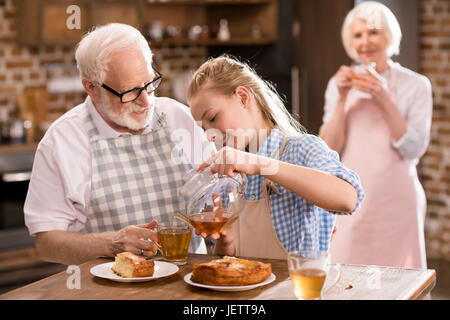 Nonni e una ragazza bere il tè con torta insieme a casa Foto Stock
