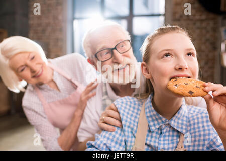 Ragazza mangiare biscotti fatti in casa con i nonni dietro Foto Stock