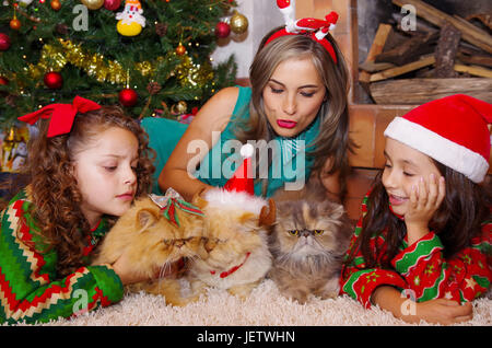 Bella famiglia indossando un abbigliamento di natale, abbracciando i suoi gatti, ricci ragazza con una cravatta rossa nei suoi capelli mentre la bruna bambina indossa un christm Foto Stock