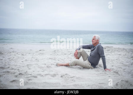 Considerato ritirato uomo seduto sulla spiaggia Foto Stock