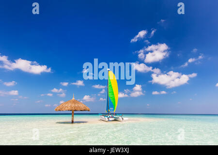 Catamarano sul sandbank tropicale isola con ombrellone. Oceano Indiano, Maldive. Blu cielo soleggiato Foto Stock