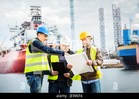 Gli ingegneri della costruzione navale presentazione della nuova soluzione in un cantiere navale. Tutti gli uomini indossano caschi di sicurezza e giubbotti di giallo. Il settore dei trasporti. Foto Stock