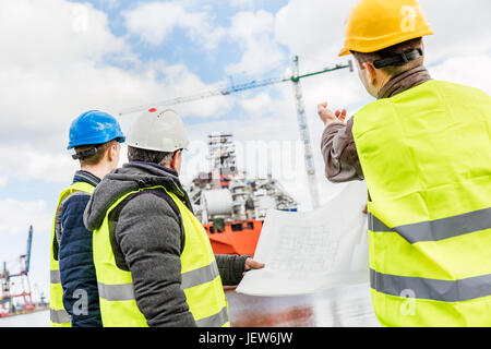 Gli ingegneri della costruzione navale presentazione della nuova soluzione in un cantiere navale. Tutti gli uomini indossano caschi di sicurezza e giubbotti di giallo. Il settore dei trasporti. Foto Stock