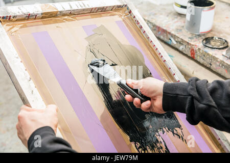 L'uomo raschiatura serigrafia in un workshop. Industria di serigrafia. Fabbricazione di lavoro. Foto Stock