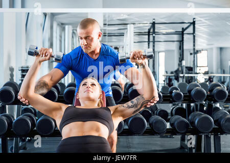 Personal trainer corregge e motiva mentre formazione bodybuilding in palestra. Un aiuto professionale durante gli allenamenti. Uno stile di vita sano e sport concept. Foto Stock