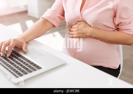 Piacevole donna incinta utilizzando computer portatile in ufficio Foto Stock