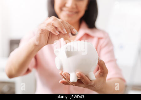 Donna positiva messa di monete in un salvadanaio Foto Stock