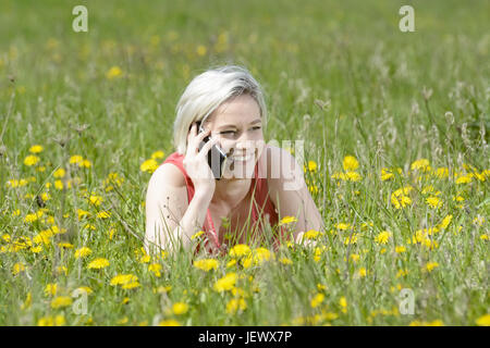 Donna con lo smartphone sul prato di fiori Foto Stock