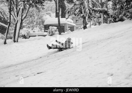 Bambino scorre sulla neve in stile vecchia scuola con un sacchetto di plastica a parco chiamato 'Macka Demokrasi - Sanat Parki' a Istanbul. La felicità e la gioia del concetto. Foto Stock