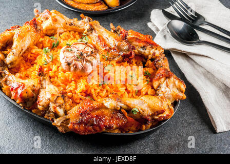 West African National cucina. Riso Jollof con grigliate di ali di pollo e banane fritte banane da cuocere.sulla pietra grigia tabella. Spazio di copia Foto Stock