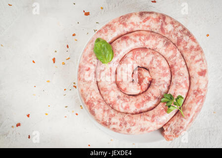 Materie salsiccia casalinga di carne bovina e suina. Su un tavolo bianco, con le spezie e le erbe aromatiche e i pomodori per la cottura. Vista dall'alto uno spazio di copia Foto Stock